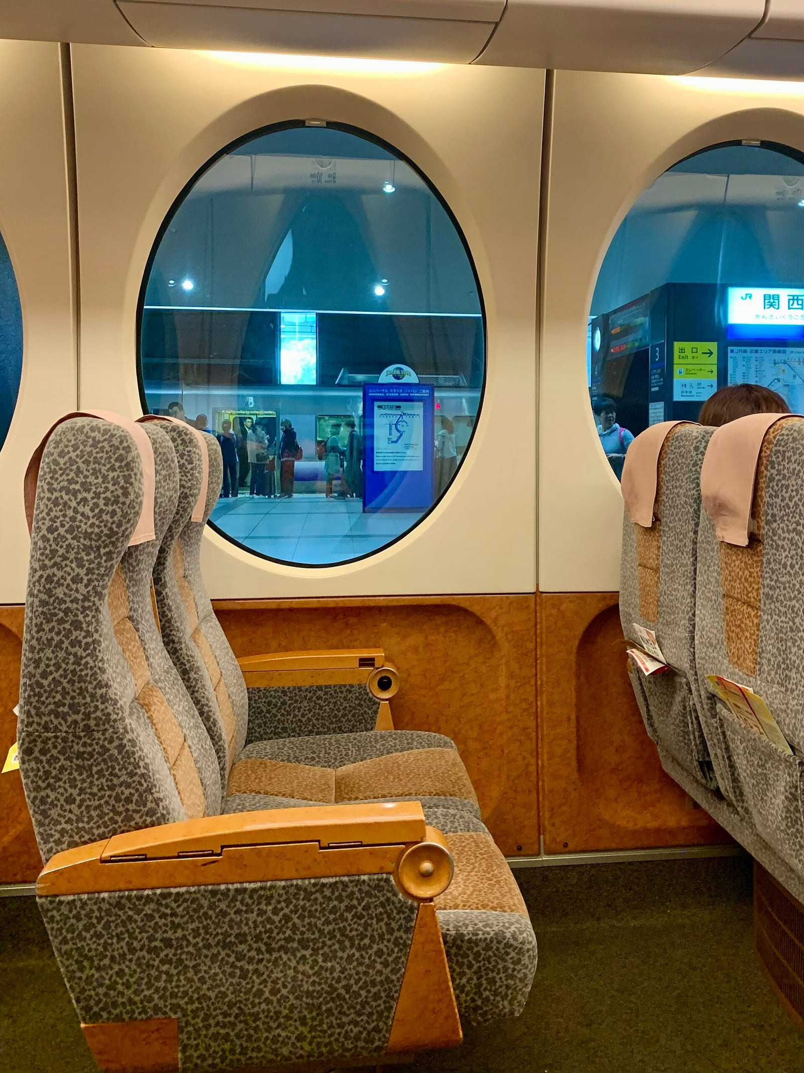 Nankai Rapi:t ekspres treninin içinde, yuvarlak pencerelerin yanında leopar desenli koltuklar sıralanıyor ve pencereden Kansai Havalimanı'ndaki peron görünüyor.