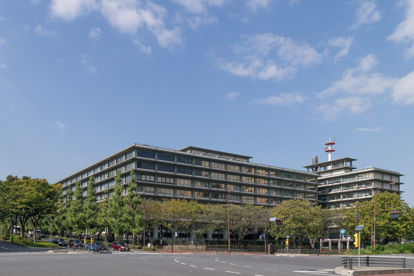 Tokyo Kasumigaseki'deki Dışişleri Bakanlığı binası, önünde ağaçlar ve yol bulunan geniş bir cephe ile açık mavi gökyüzü altında görülüyor.