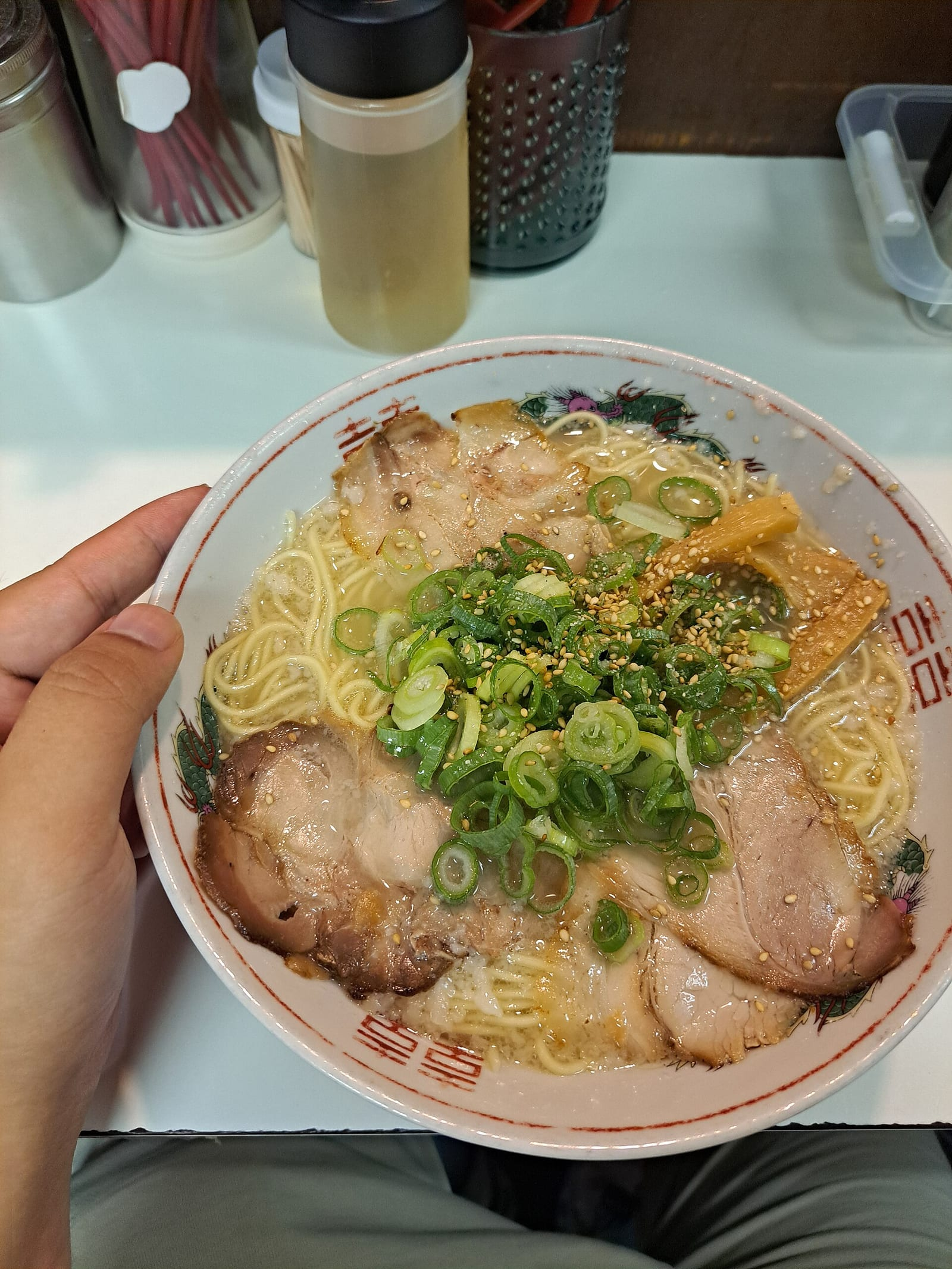 Kyoto'daki bir ramen barında, pirzola dilimleri, taze yeşil soğan ve susamla süslenmiş, desenli beyaz kasede servis edilen sıcak shio ramen çorbası görünüyor.