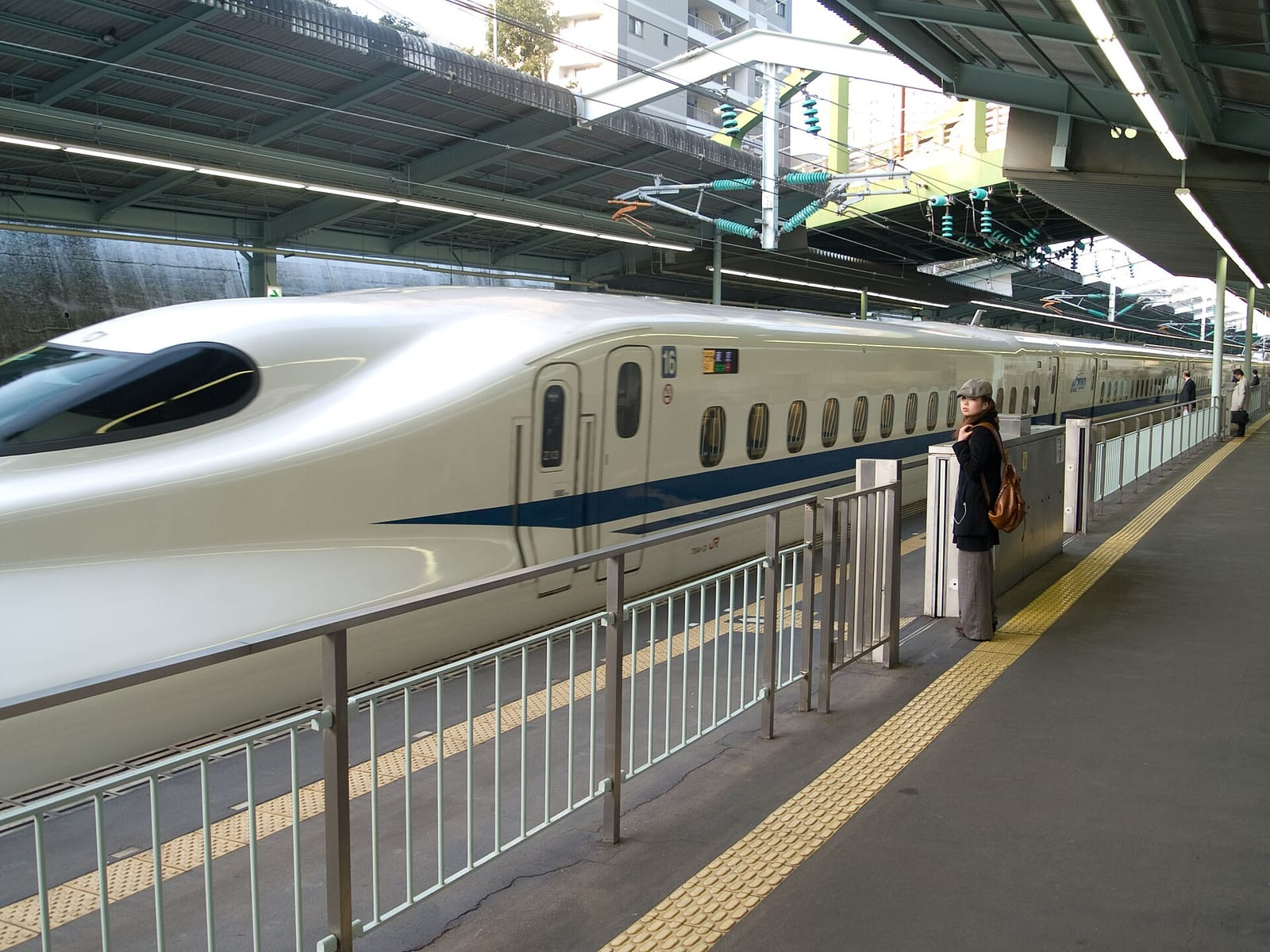 Shin-Kobe istasyonunda peronda bekleyen beyaz-mavi N700 serisi Nozomi hızlı treni ve yanında uzaktan görünen tek bir yolcu.