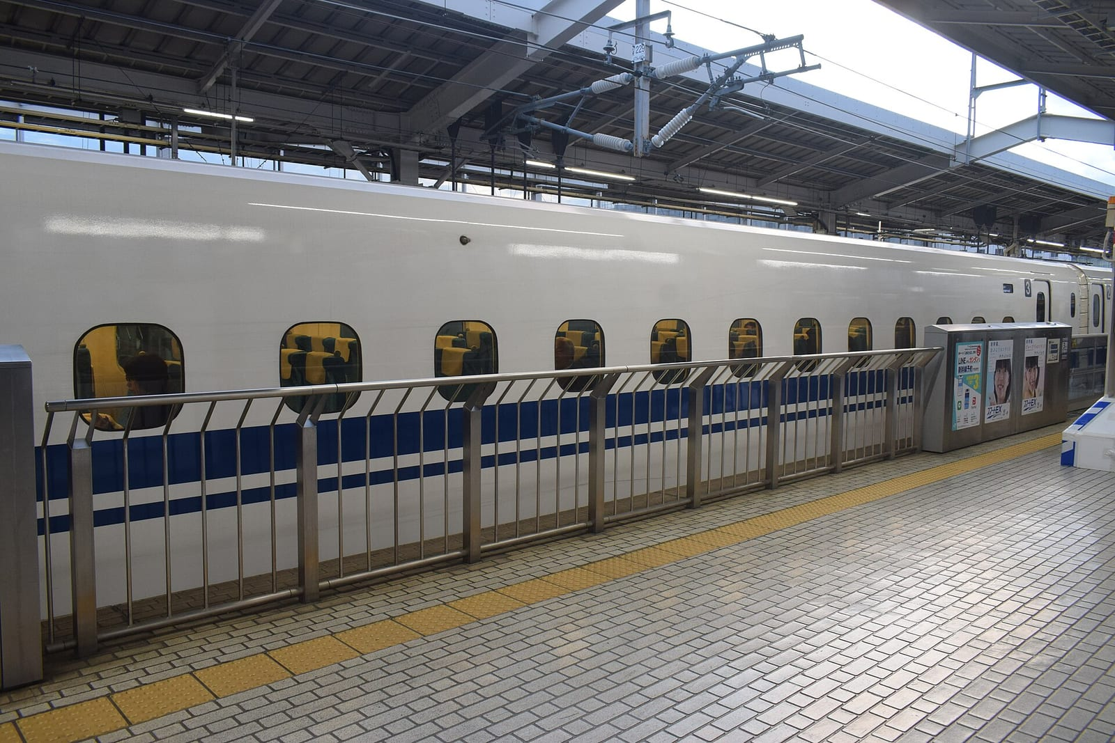 Kyoto İstasyonu'nda peronda duran beyaz-mavi renkli Tokaido Shinkansen treninin uzun gövdesi ve pencereleri görülüyor.