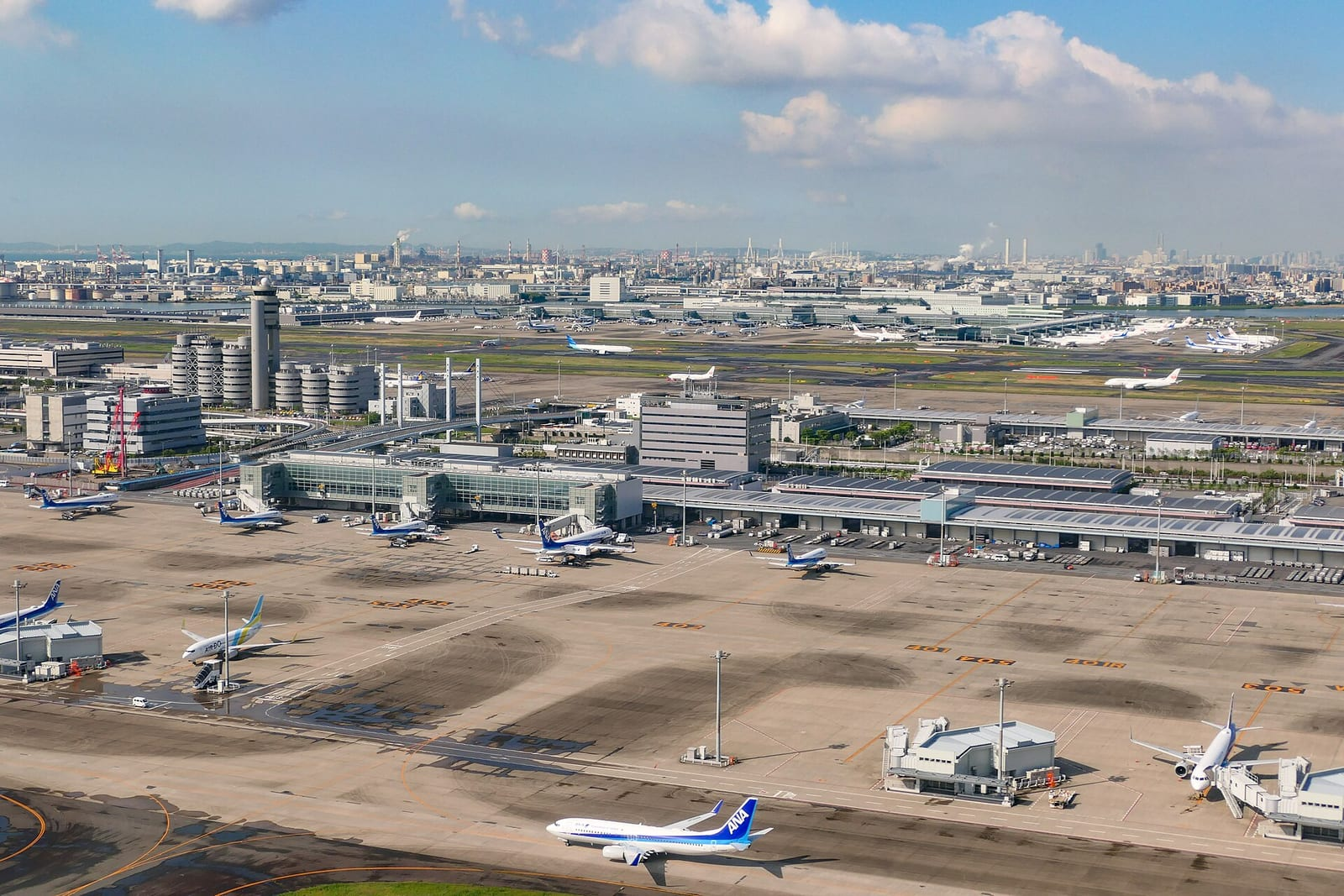 Tokyo Haneda Havalimanı'nın 2. Terminal uydu binası ve çevresindeki park halindeki uçaklar, açık mavi gökyüzü altında yukarıdan görülüyor.