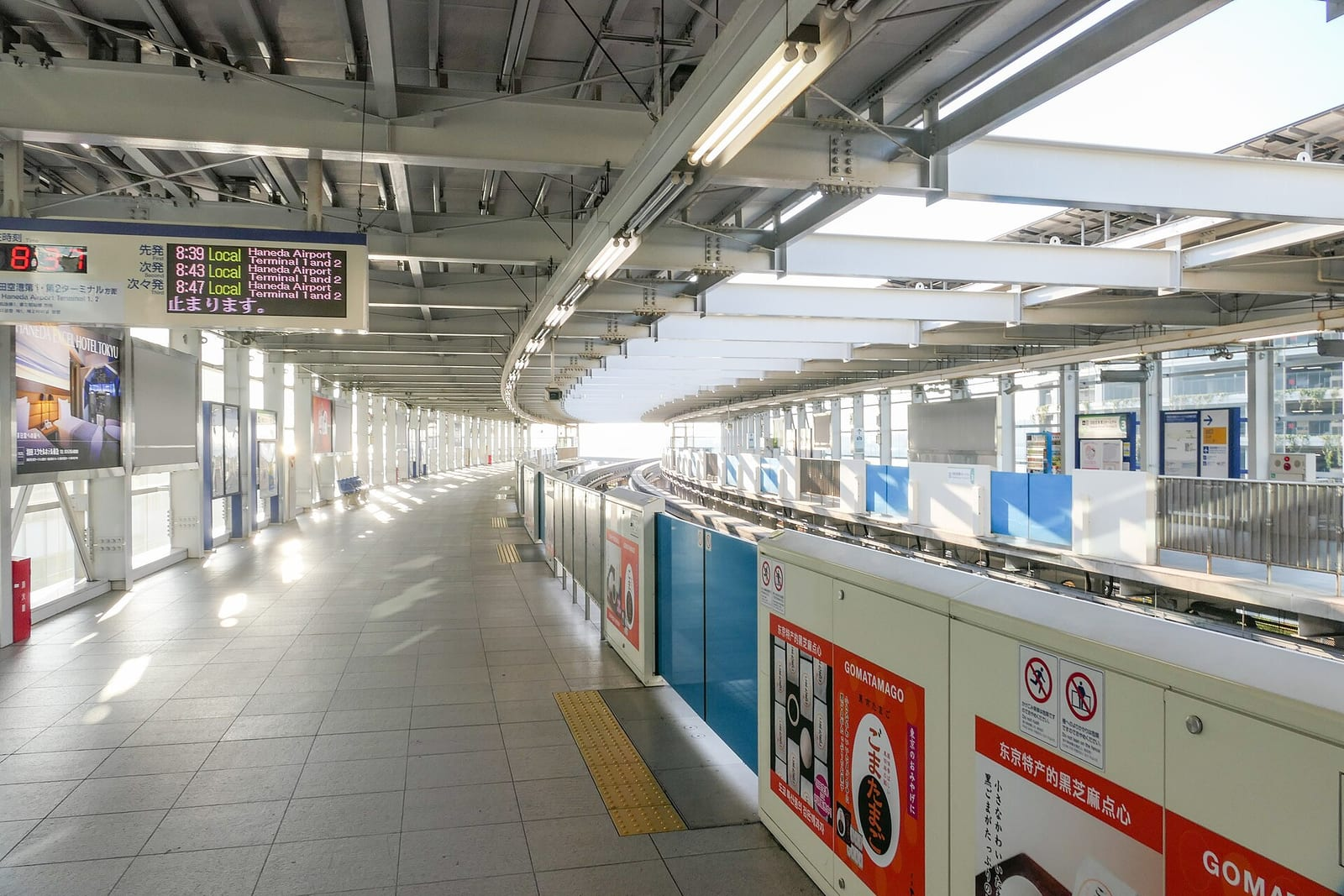 Haneda Havalimanı Terminal 3 istasyonunda Tokyo Monorail peronu, boş ve aydınlık bir şekilde uzanıyor, yanda mavi bölme panelleri var.