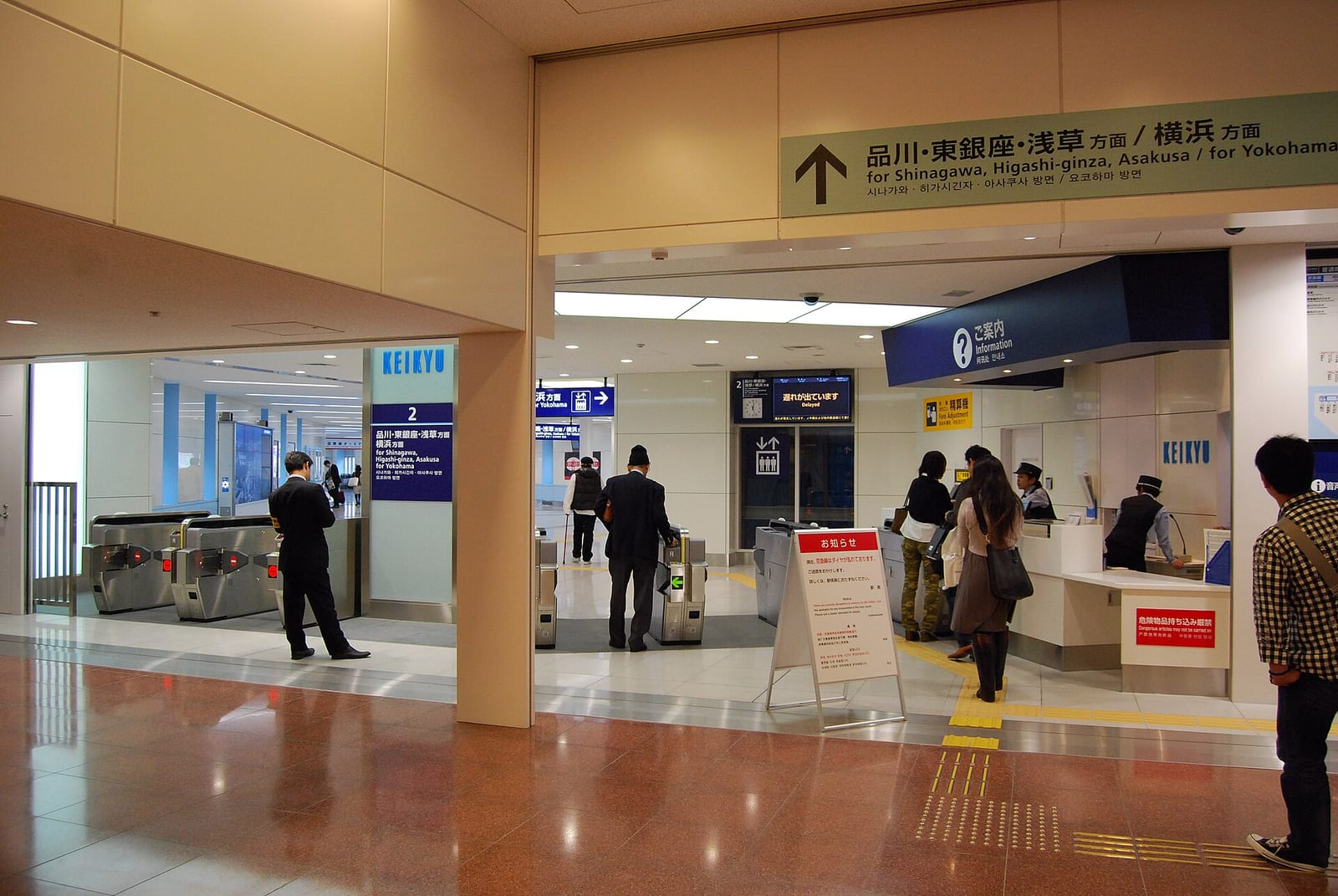 Haneda Havalimanı Uluslararası Terminal istasyonunda Keikyu hattının turnikeleri, bilet gişesi ve Japonca-İngilizce yön tabelaları görülüyor.