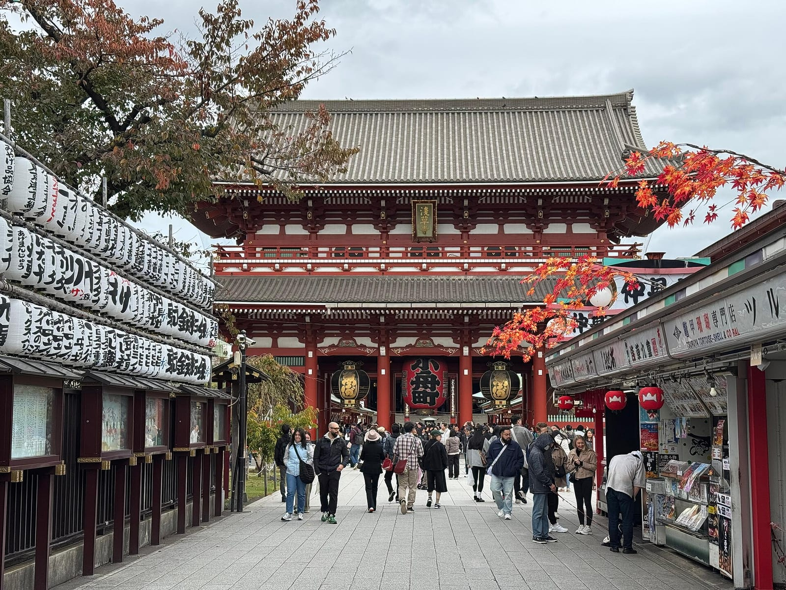 Tokyo Asakusa'daki Sensoji tapınağının geniş çatılı ana salonu, önünde yürüyen ziyaretçiler ve mavi gökyüzü görülüyor.