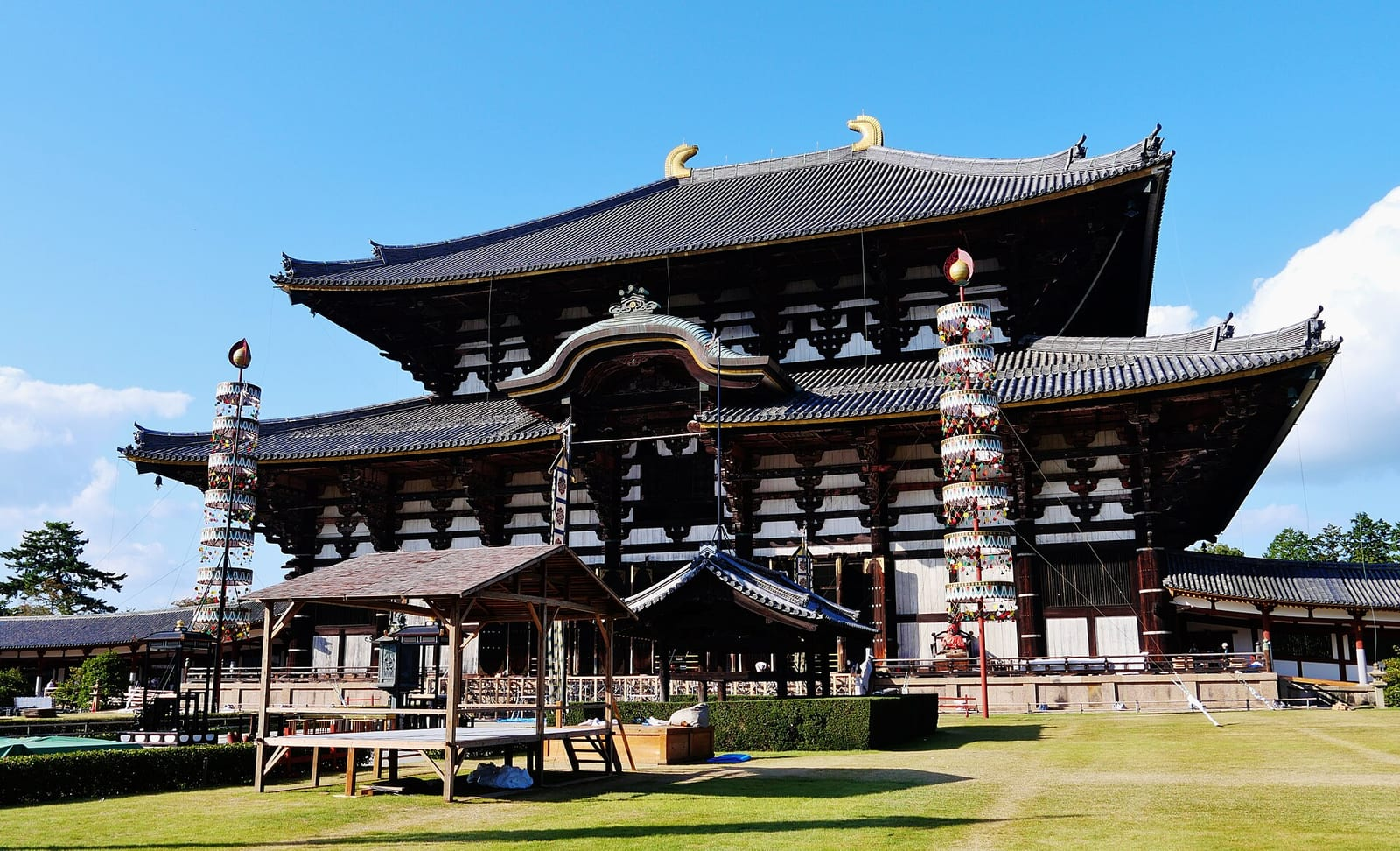 Nara'daki Todai-ji Tapınağı'nın devasa ahşap Daibutsuden (Büyük Buda Salonu) yapısı, mavi gökyüzü ve yeşil çimenlerin önünde yan taraftan görünüyor.