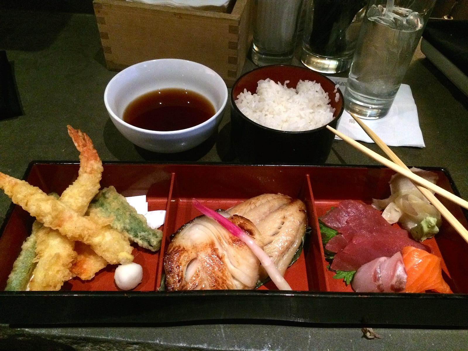 Japon restoranında bir tepside tempura karides ve sebzeler, ızgara balık, çiğ balık dilimleri, pirinç ve sos kasesi birlikte servis ediliyor.