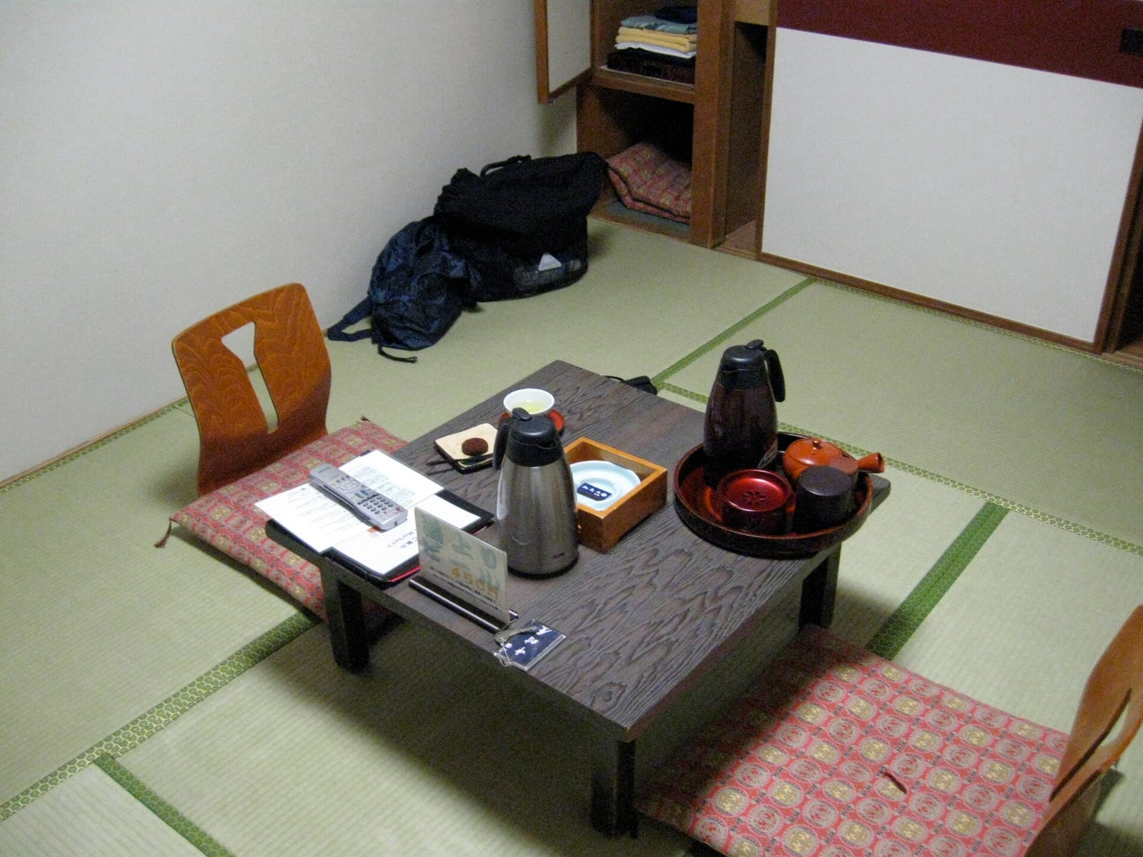 Geleneksel bir Japon ryokan odasında tatami zemin üzerinde alçak bir masa, çay takımı, termos ve iki yer minderi bulunuyor.