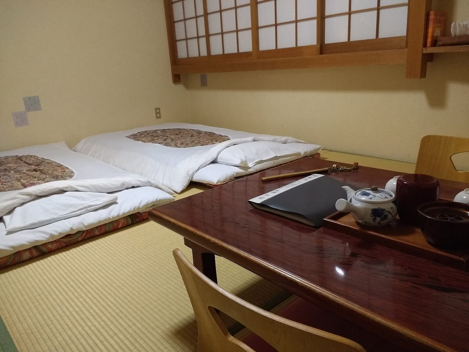 Tatami zeminli geleneksel bir ryokan odasında yere serilmiş iki futon yatak, alçak bir masa ve çay takımı görünüyor.