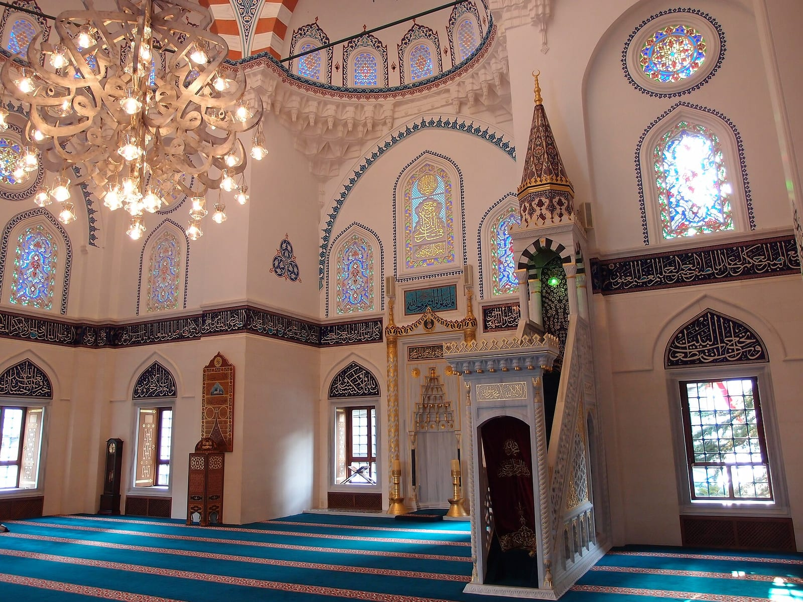 Tokyo Camii'nin ışıklı avizeli, vitraylı pencereli ve minberli iç mekânı, mavi halıyla kaplı geniş bir namaz salonunu gösteriyor.