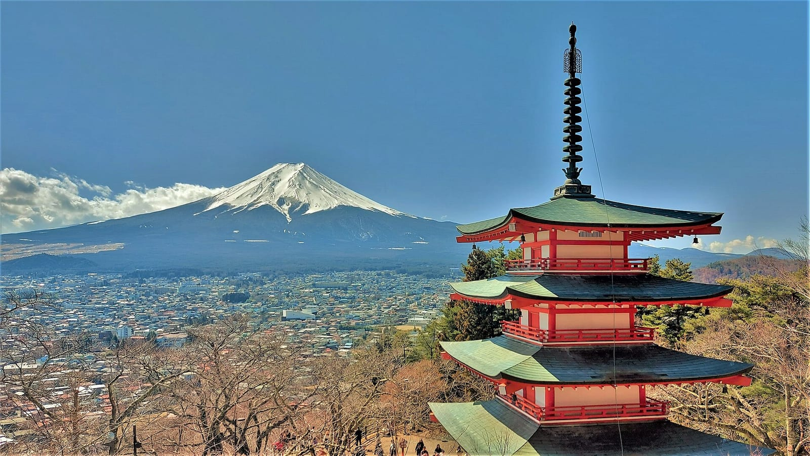 Kırmızı Chureito Pagodası'nın arkasında karla kaplı Fuji Dağı, mavi gökyüzü ve altında Fujiyoshida kasabası görülüyor.