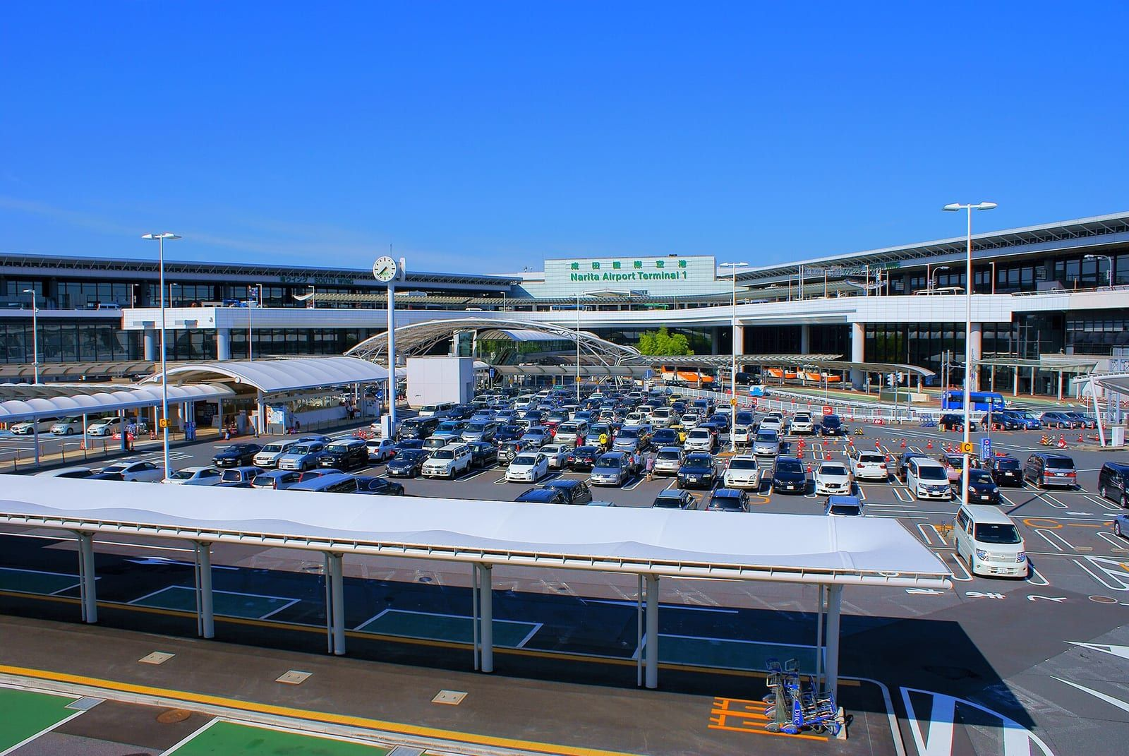 Narita Uluslararası Havalimanı Terminal 1'in önünde otopark, taksi ve otobüs alanı ile mavi gökyüzü altında terminal binası