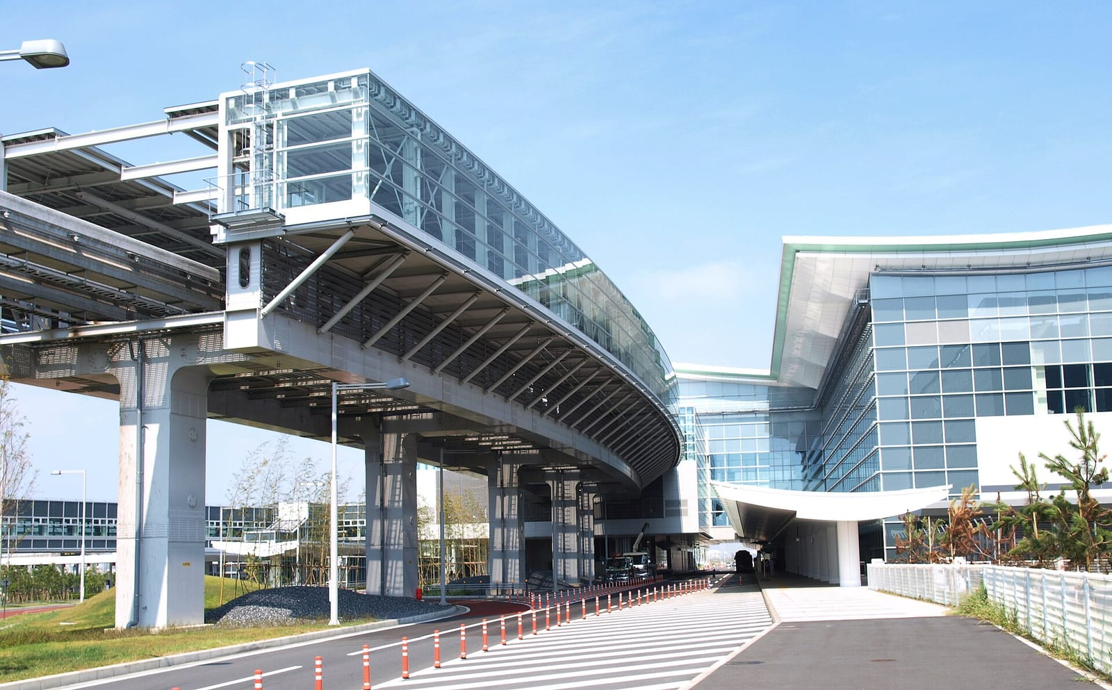 Haneda Havalimanı uluslararası terminali yakınında, cam cepheli binaya uzanan yükseltilmiş monoray hattı ve mavi gökyüzü görülüyor.